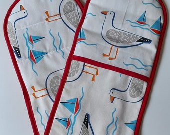 Double oven gloves / pot holder in thick cotton, padded  in Whitby Seagull  design in white with splashes of red and blue, trimmed in red.