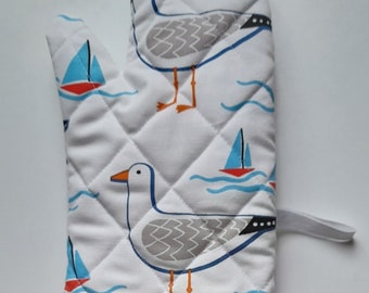 A stylish quilted padded oven glove / oven mitt / pot holder in organic cotton in whitby seagull  design  on white background.