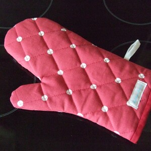 May include: A red quilted oven glove with a white polka dot design. It has a hanging loop and a label. This kitchen essential is designed to protect hands from heat when cooking.