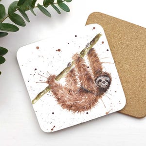 May include: A white coaster featuring a brown sloth hanging upside down from a branch. The sloth has a brown and white face and is surrounded by brown splatters.