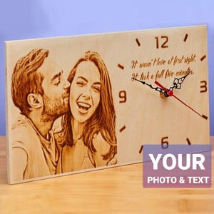 May include: A wooden clock with a laser-engraved image of a couple. The clock face has black hands and Roman numerals. The text "It wasn't love at first sight. It took a full five minutes." is engraved below the clock face. The text "YOUR PHOTO & TEXT" is printed below the clock.