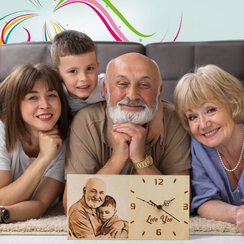 May include: A wooden clock with a photo of a man and a child, and the words "Love You" engraved on the clock face. The clock has black hands and a light-colored wooden frame. The clock is in front of a family.