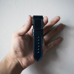 May include: A dark blue leather watch strap with light blue stitching. The strap has a pointed end and is designed for a watch with a standard lug width.