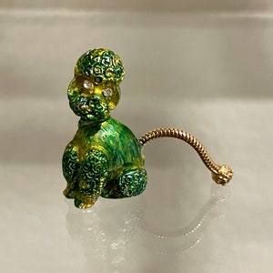 May include: A green and gold enamel poodle brooch with rhinestone eyes. The poodle is sitting with its tail curled up behind it.