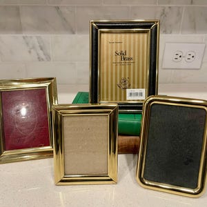 May include: Four decorative picture frames with gold and black borders. One frame has a red interior, another has a tan interior, and a third has a black interior. The fourth frame has a black border and a striped interior. The frames are of varying sizes.