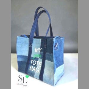Könnte beinhalten: Jeans-Tote-Tasche mit Patchwork-Design in verschiedenen Blautönen. Die Tasche hat lange Henkel und den Text "MY green TOTE BAG" in Weiß und Grün. Das Markenlogo "SL SCHICKI LINE" befindet sich unten.