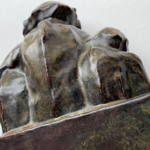 May include: A ceramic sculpture of two figures, one seated and the other standing, both with a dark green glaze. The sculpture is on a rectangular base.