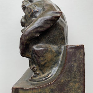 May include: A ceramic sculpture of a monkey holding a smaller monkey. The sculpture is a dark green color with brown accents. The sculpture is on a square base.