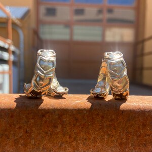 May include: A pair of gold-toned hoop earrings with a geometric design. The earrings are made of interlocking pieces that form a series of triangles.