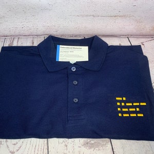 May include: A navy blue polo shirt with a yellow embroidered design on the right side. The design is a series of horizontal lines. The shirt has a button-up collar and a tag that reads "Embroidered Memories".