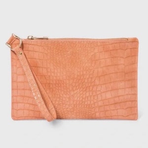 May include: A peach-colored clutch purse with a crocodile-embossed texture and a gold zipper. The purse has a wrist strap.