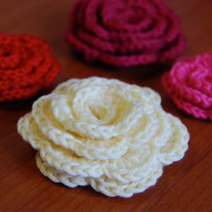 May include: Four crocheted flowers in different colors: red, pink, white, and a darker pink. The flowers are all made with the same stitch pattern and have a similar shape.