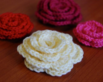 May include: Four crocheted flowers in different colors: red, pink, white, and a darker pink. The flowers are all made with the same stitch pattern and have a similar shape.
