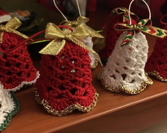 May include: Five crocheted bell ornaments in red and white with gold trim. The bells are decorated with bows made of gold and green ribbon.