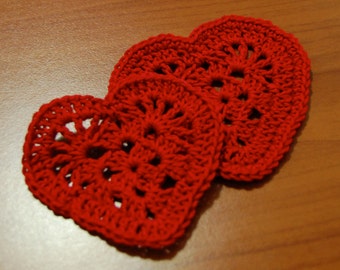 May include: Two red crocheted hearts, one slightly larger than the other, are arranged on a wooden surface. The hearts are made with a delicate openwork pattern.
