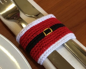 Peut inclure: Un rond de serviette en crochet rouge avec une bordure blanche en haut et en bas, une bande noire horizontale au centre et un petit détail de boucle rectangulaire jaune au milieu, entourant une serviette blanche et des couverts.
