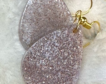 May include: A pair of teardrop-shaped earrings with a silver glitter finish and gold hooks. The earrings are on a white surface.