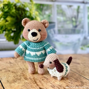 Peut inclure: Un ours en peluche crocheté marron portant un pull turquoise et blanc à motif de cœur se tient à côté d'un chien crocheté marron et blanc portant un pull turquoise et blanc avec un col marron.