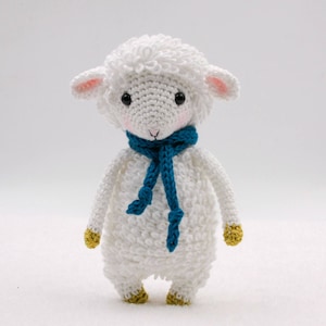 May include: White crocheted lamb toy with a blue scarf and yellow feet.