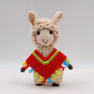 May include: A crocheted llama wearing a red, green, and yellow poncho. The llama has a white face with black eyes and a black nose.