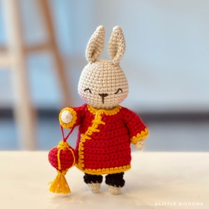 May include: A crocheted rabbit wearing a red and yellow Chinese-style outfit and holding a red and yellow lantern.