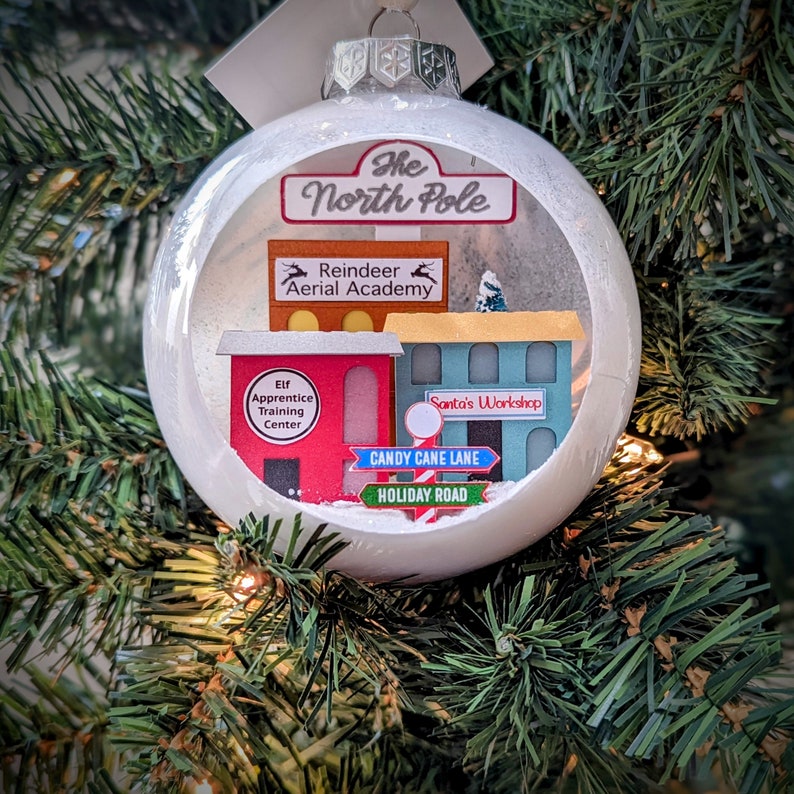A diorama ornament featuring scenes from the North Pole such as Santa's Workshop, Elf Apprentice Training Center and Reindeer Aerial Academy