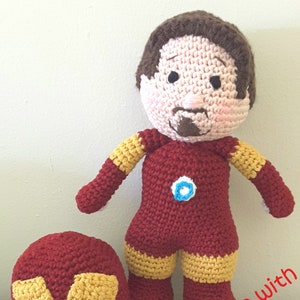 May include: Handmade crocheted Iron Man doll with a removable mask. The doll is red and yellow with a blue arc reactor on the chest. The mask is red and yellow with a white face.