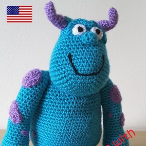 May include: A blue crocheted monster with purple spots and horns. The monster has a big smile and white eyes. The text "Handmade with Love..." is written in red on the bottom right corner of the image.