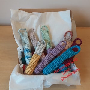 May include: A box filled with colorful crocheted finger puppets. The puppets are made with different colored yarn and have a variety of designs. The box is lined with white tissue paper and the text "Handmade with Love... Shoppysgifts" is visible on the side of the box.