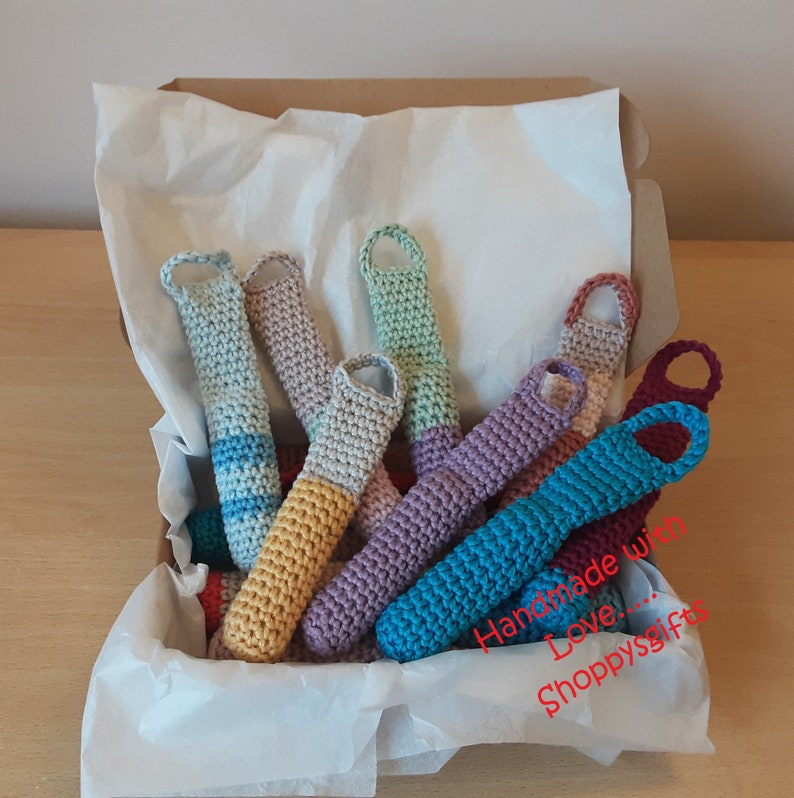 May include: A box filled with colorful crocheted finger puppets. The puppets are made with different colored yarn and have a variety of designs. The box is lined with white tissue paper and the text "Handmade with Love... Shoppysgifts" is visible on the side of the box.