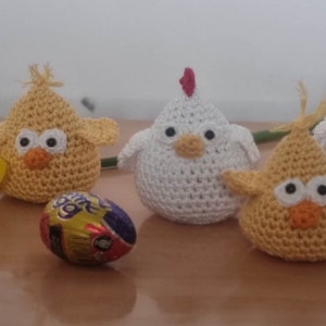 Può includere: Quattro pulcini all'uncinetto, due gialli e due bianchi, con occhi neri e becchi arancioni. Un pulcino giallo tiene un uovo di cioccolato.
