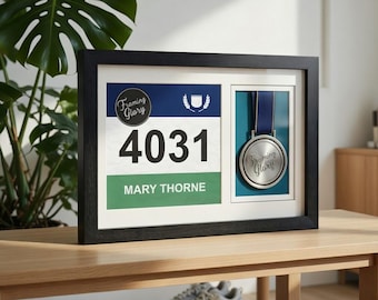 May include: A framed display with a race bib and medal. The black frame contains a white mount with a blue and green race bib, showing the number 4031 and the name Mary Thorne. A silver medal with a blue ribbon is also displayed.
