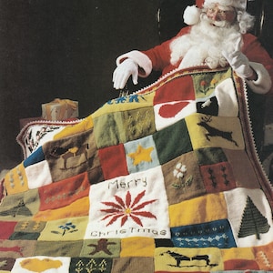 May include: Santa Claus sits in a chair with a colorful knitted patchwork blanket. The blanket features a variety of holiday-themed designs, including a star, a heart, a tree, and a reindeer. The blanket also has the words "Merry Christmas" knitted into it.