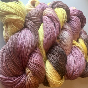 May include: A skein of yarn with three colors: a light yellow, a light purple, and a brown. The yarn is twisted together in a braid.