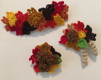 May include: A set of three crocheted fall leaf ornaments in shades of red, orange, yellow, brown, and green. The ornaments are made of yarn and are shaped like leaves. They are perfect for decorating for the fall season.