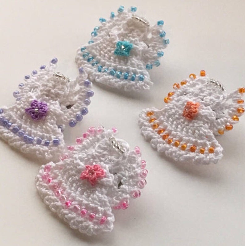 May include: Four crocheted angel ornaments with beaded trim. Each angel is white with a different colored flower in the center. The flowers are purple, blue, orange, and pink.