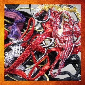 May include: A close-up of a collection of decorative ribbons and trims in various colors. Red, black, gold, silver, and purple ribbons are intertwined. Some ribbons have sequins or intricate patterns, creating a textured and visually rich display.