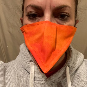 May include: A person wearing a gray hoodie with a bright orange face mask. The mask is triangular in shape and has a black trim.