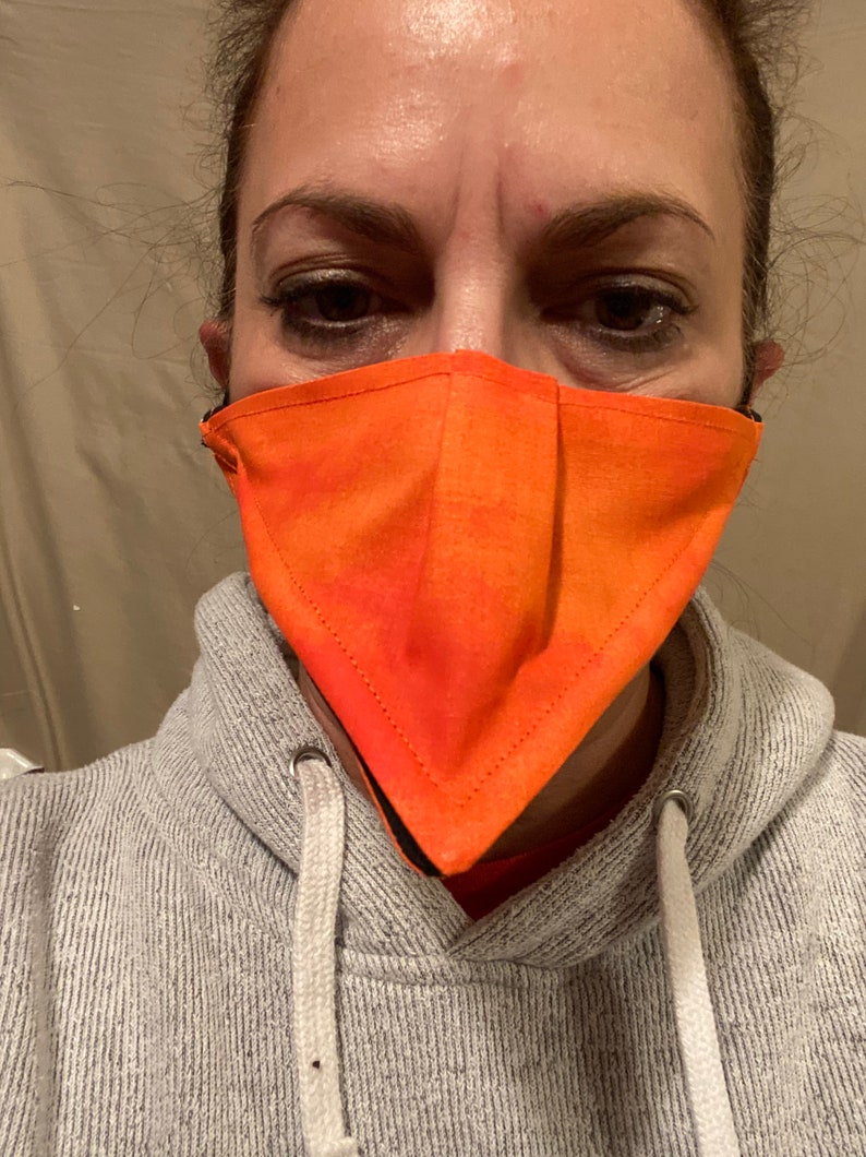 May include: A person wearing a gray hoodie with a bright orange face mask. The mask is triangular in shape and has a black trim.