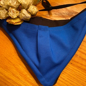 May include: A blue face mask with black elastic straps and a white flower embellishment.