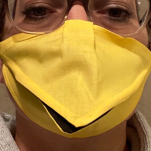 May include: A person wearing a yellow face mask with a black lining. The mask has a unique design with a pointed bottom.