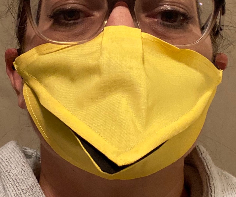 May include: A person wearing a yellow face mask with a black lining. The mask has a unique design with a pointed bottom.