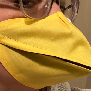 May include: A yellow fabric face mask with a black trim and a beak-like extension. The mask is worn by a person.