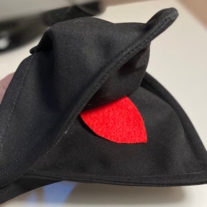 May include: Black fabric hat with a red felt tongue sticking out. The hat is folded in half and the tongue is visible.