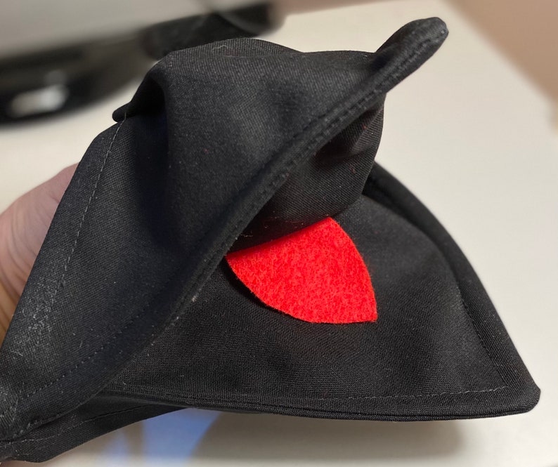 May include: Black fabric hat with a red felt tongue sticking out. The hat is folded in half and the tongue is visible.