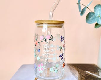 May include: A clear glass tumbler with a bamboo lid and a clear glass straw. The tumbler is decorated with colorful floral designs and the text "Consider how the wildflowers grow Luke 12:27-28".