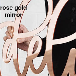 May include: Rose gold mirror letters spelling out the word "Welcome".
