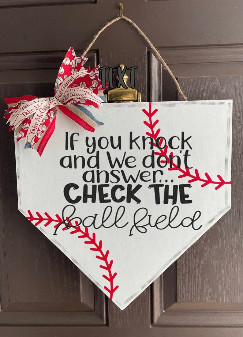 May include: White baseball home plate-shaped sign with red stitching and the text "If you knock and We don't answer... CHECK THE ball field." A red, white, and blue bow is attached to the top. A baseball-themed decorative item.