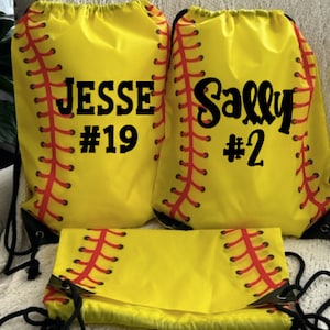 May include: Two yellow drawstring bags with a softball design. One bag says "Jesse #19" and the other says "Sally #2".