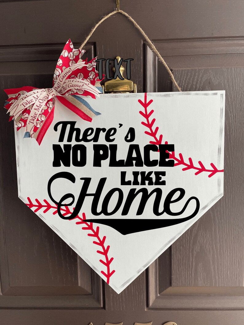 May include: A baseball-themed home decor sign shaped like home plate. The white sign features red stitching, the phrase "There's NO PLACE LIKE Home" in black, and a decorative bow with baseball and text patterns.